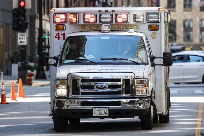 A Chicago Fire Department ambulance rushes through downtown, symbolizing the unseen emergencies caused by economic strain—including rising crime and violence linked to the social impact of tariffs and inflation.