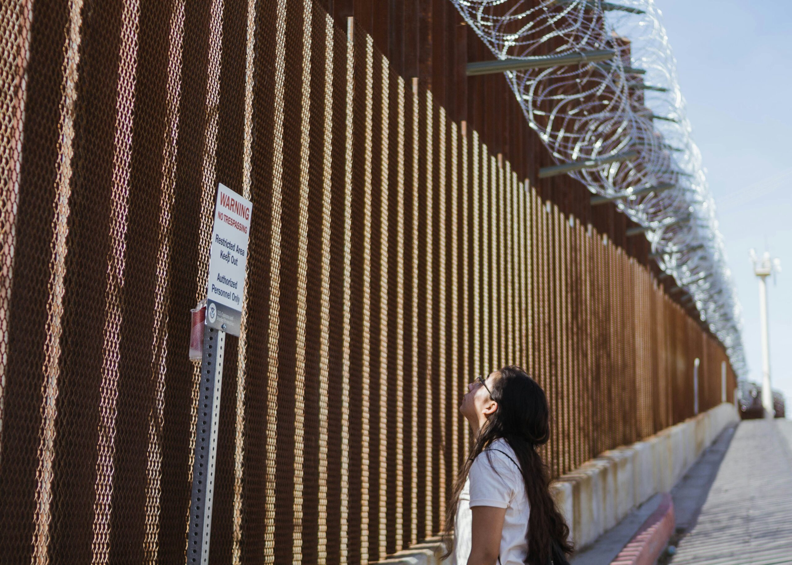Woman looking at a sign posted at the US-Mexico Border, 2025.